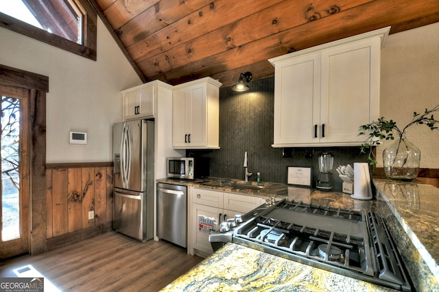 kitchen featuring lofted ceiling, sink, stainless steel appliances, white cabinets, and dark stone counters