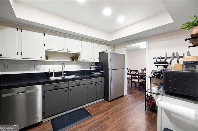 kitchen featuring dark wood-type flooring, sink, a tray ceiling, stainless steel appliances, and white cabinets