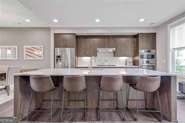 kitchen featuring appliances with stainless steel finishes, a kitchen island with sink, sink, and a breakfast bar area