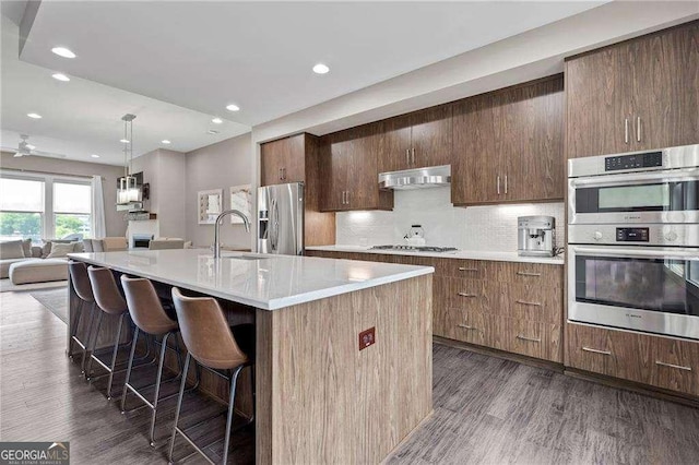 kitchen with sink, a breakfast bar, a kitchen island with sink, backsplash, and stainless steel appliances