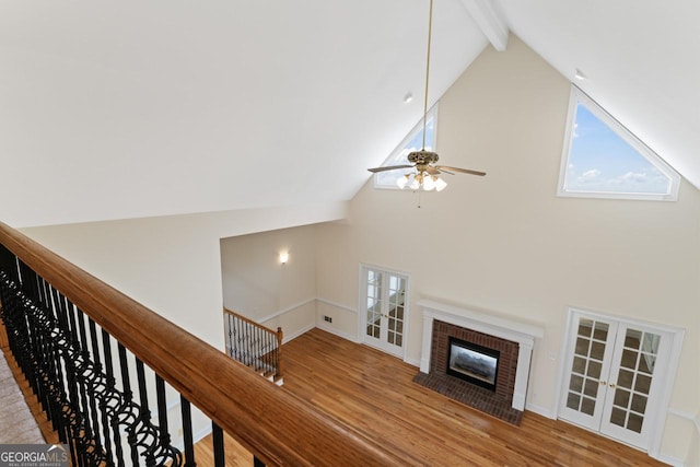 living room featuring ceiling fan, high vaulted ceiling, a brick fireplace, beamed ceiling, and light wood-type flooring