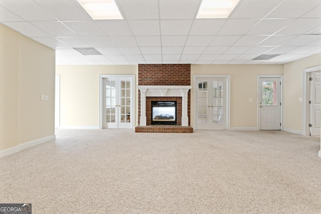 unfurnished living room featuring a paneled ceiling, light carpet, a fireplace, and french doors