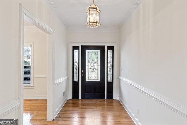 foyer entrance with wood-type flooring, ornamental molding, and a chandelier