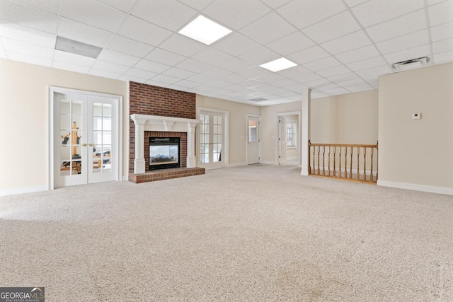 unfurnished living room with a drop ceiling, a brick fireplace, french doors, and carpet flooring