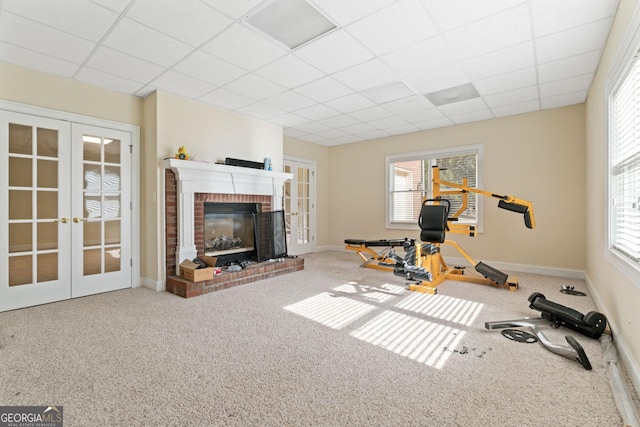 workout room featuring french doors, a healthy amount of sunlight, a fireplace, and a drop ceiling