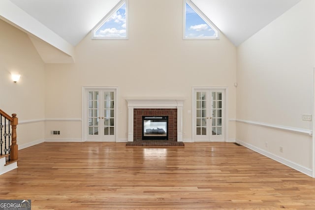 unfurnished living room with a brick fireplace, french doors, and light wood-type flooring