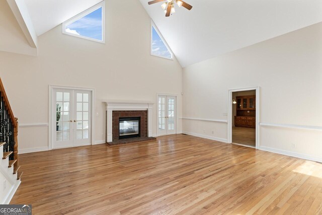 unfurnished living room featuring a brick fireplace, light hardwood / wood-style floors, french doors, and ceiling fan