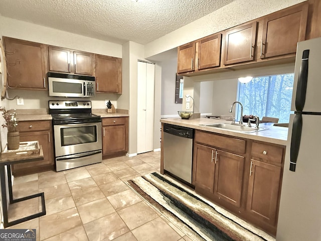 kitchen featuring stainless steel appliances, sink, light tile patterned floors, and a textured ceiling