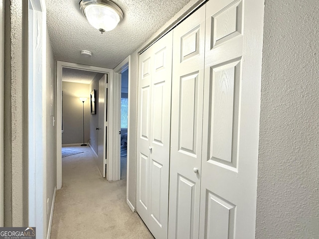 hall featuring light colored carpet and a textured ceiling