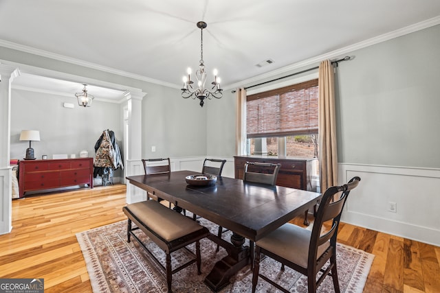 dining room with ornamental molding, light hardwood / wood-style floors, decorative columns, and a notable chandelier