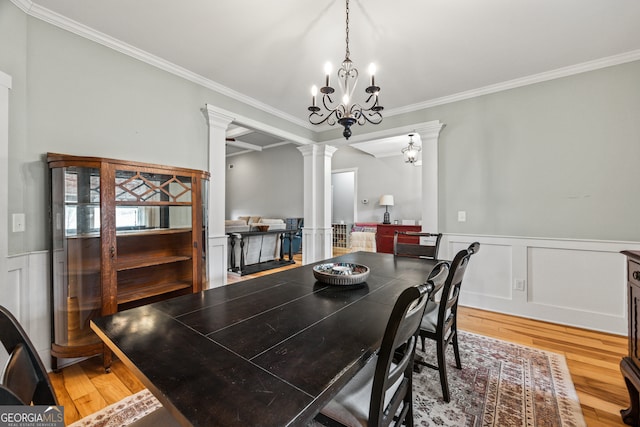 dining room featuring crown molding, a notable chandelier, wood-type flooring, and ornate columns