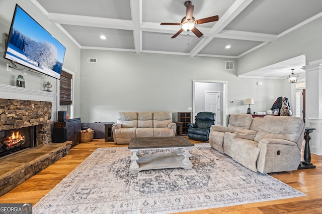 living room featuring a stone fireplace, beamed ceiling, ornamental molding, coffered ceiling, and light wood-type flooring