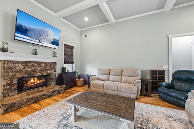 living room featuring crown molding, beam ceiling, coffered ceiling, light hardwood / wood-style floors, and a stone fireplace