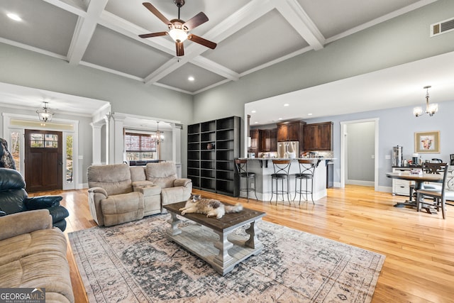 living room with ceiling fan with notable chandelier, decorative columns, beamed ceiling, coffered ceiling, and light hardwood / wood-style flooring