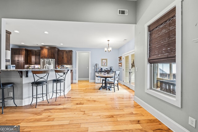 kitchen featuring a breakfast bar area, stainless steel refrigerator, dark brown cabinets, a notable chandelier, and light hardwood / wood-style floors