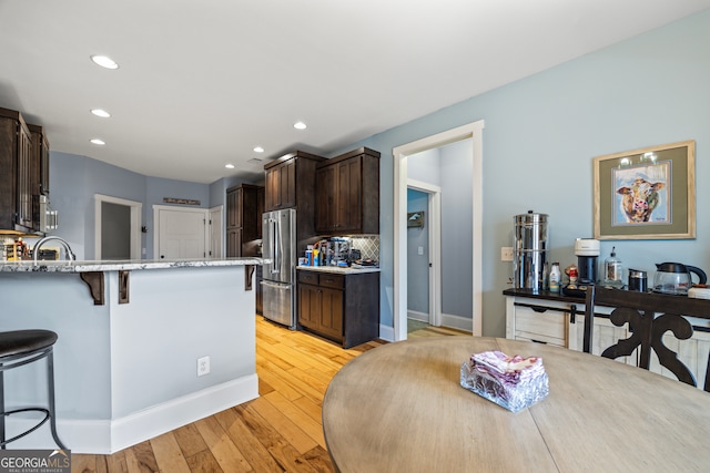 kitchen featuring a kitchen bar, dark brown cabinets, light hardwood / wood-style flooring, stainless steel appliances, and backsplash