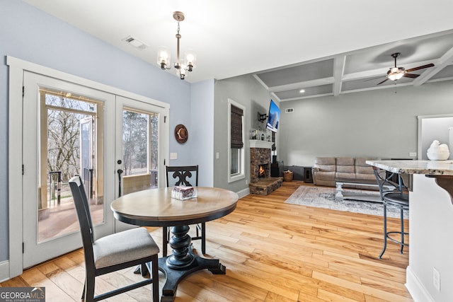 dining space with coffered ceiling, a stone fireplace, wood-type flooring, and beam ceiling