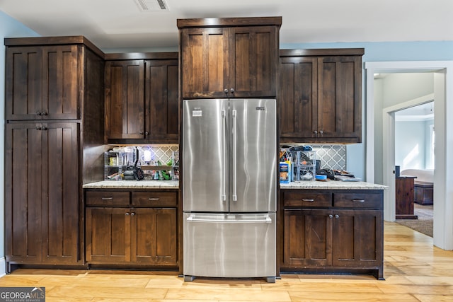 kitchen featuring high end fridge, dark brown cabinets, light stone countertops, and light hardwood / wood-style flooring