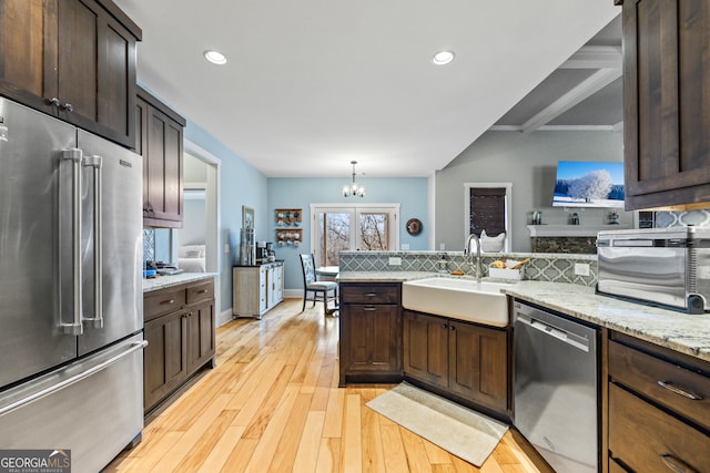 kitchen with sink, hanging light fixtures, stainless steel appliances, dark brown cabinetry, and light wood-type flooring