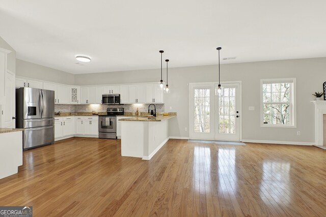 kitchen featuring appliances with stainless steel finishes, pendant lighting, tasteful backsplash, white cabinetry, and kitchen peninsula