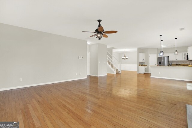 unfurnished living room featuring ceiling fan with notable chandelier and light wood-type flooring