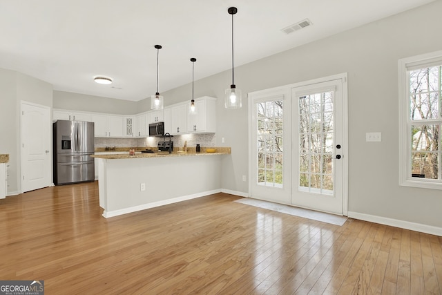 kitchen featuring white cabinetry, appliances with stainless steel finishes, kitchen peninsula, light stone countertops, and decorative backsplash