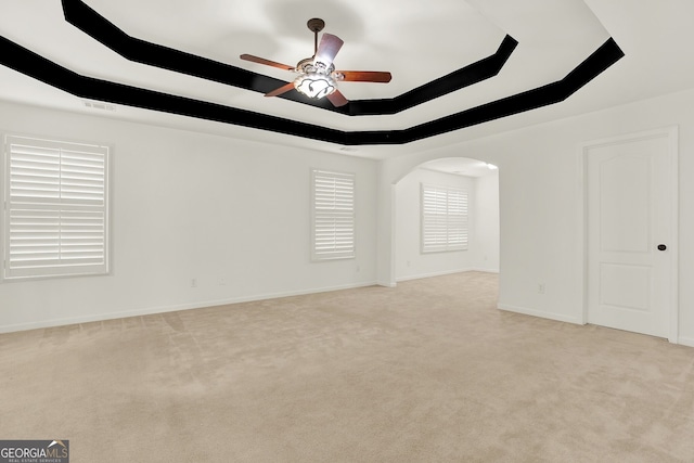 empty room with light colored carpet, a raised ceiling, and ceiling fan