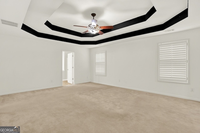 spare room featuring a raised ceiling, light carpet, and ceiling fan