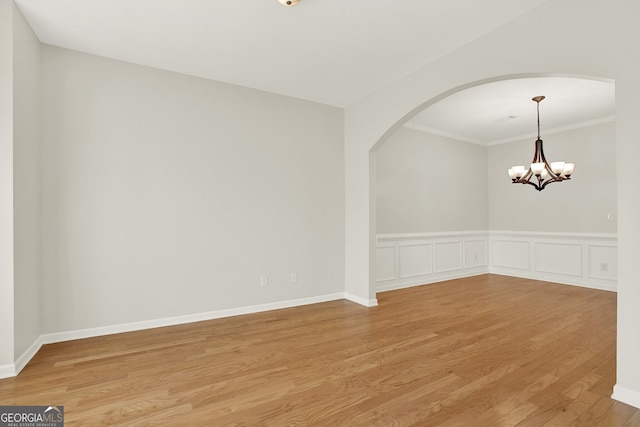 empty room with crown molding, a chandelier, and light hardwood / wood-style flooring