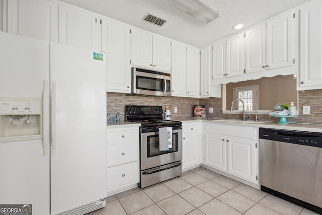 kitchen with light tile patterned flooring, sink, white cabinetry, stainless steel appliances, and backsplash