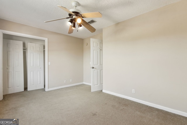 unfurnished bedroom with light carpet, ceiling fan, a closet, and a textured ceiling