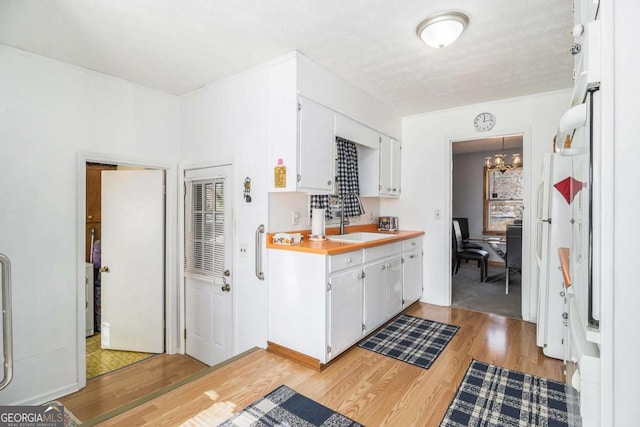 kitchen with white cabinetry, sink, a chandelier, and light wood-type flooring