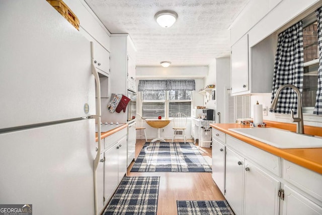 kitchen with sink, light wood-type flooring, white cabinets, white fridge, and a textured ceiling