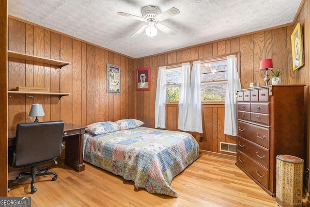 bedroom featuring wooden walls, a textured ceiling, and light hardwood / wood-style flooring