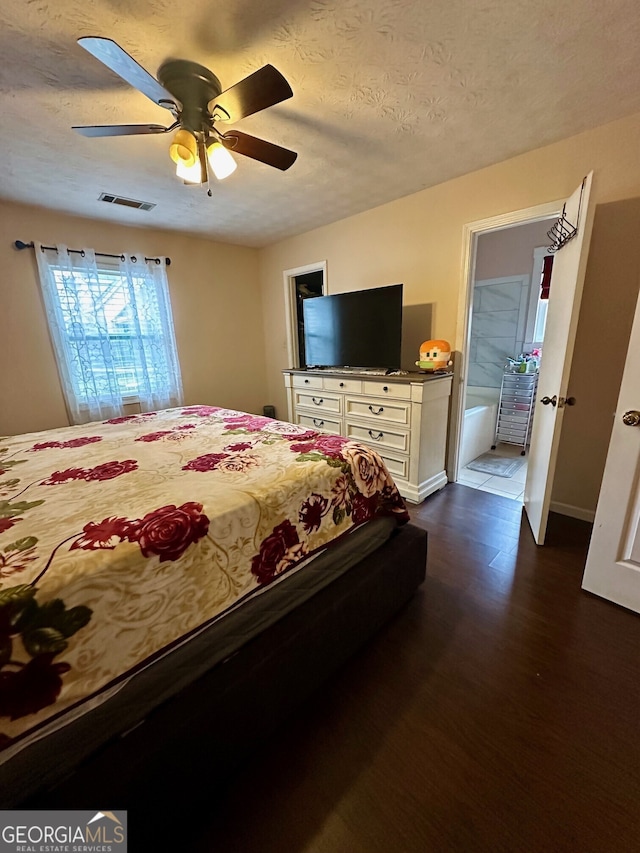 bedroom featuring ceiling fan, ensuite bath, dark hardwood / wood-style floors, and a textured ceiling