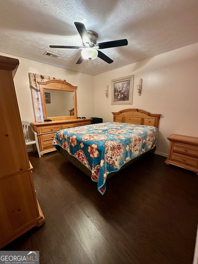 bedroom with ceiling fan, dark wood-type flooring, and a textured ceiling