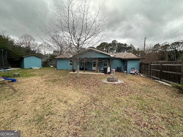 rear view of property with central air condition unit, a trampoline, a yard, a storage unit, and a patio