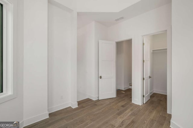 unfurnished bedroom featuring dark wood-type flooring, a walk in closet, and a closet