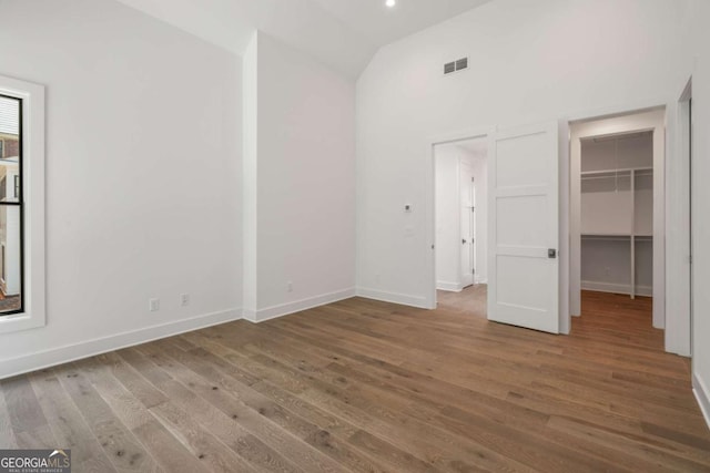 unfurnished bedroom featuring lofted ceiling, wood-type flooring, a closet, and a walk in closet