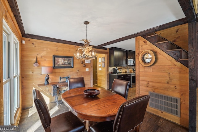 dining room featuring dark hardwood / wood-style flooring, wooden walls, and an inviting chandelier