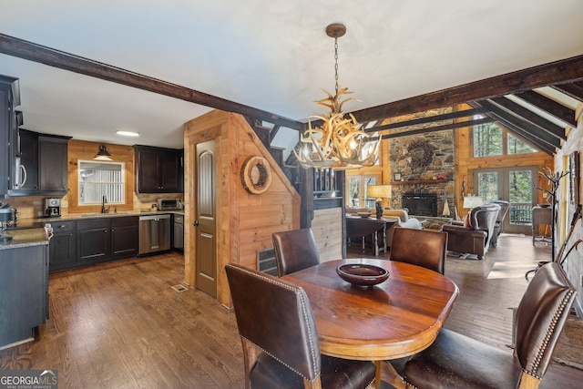 dining room with a stone fireplace, vaulted ceiling with beams, sink, dark hardwood / wood-style flooring, and a notable chandelier