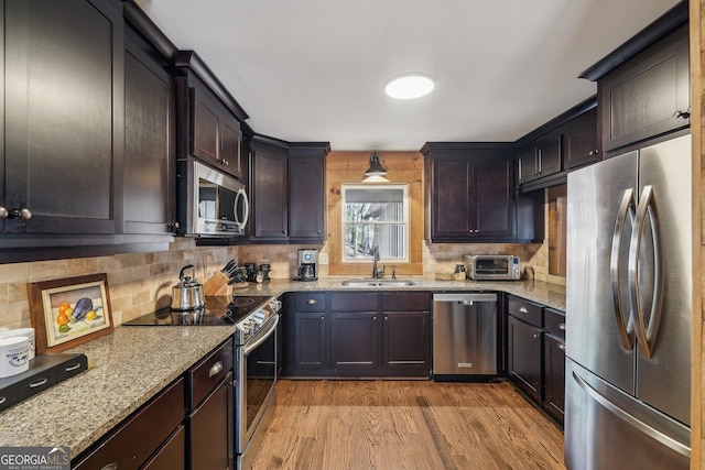 kitchen featuring sink, appliances with stainless steel finishes, dark brown cabinets, light stone countertops, and light wood-type flooring