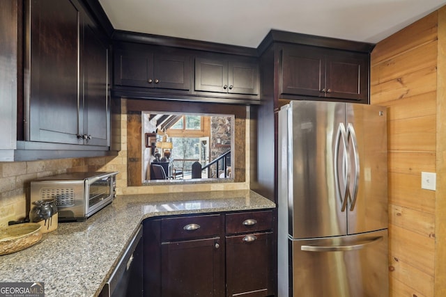 kitchen featuring stainless steel refrigerator, dark brown cabinetry, light stone countertops, and backsplash