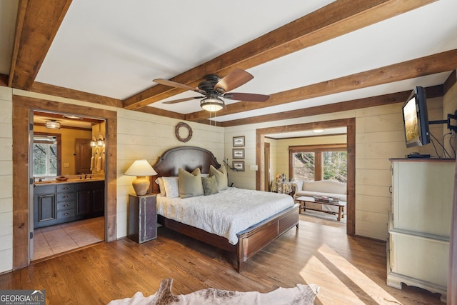 bedroom featuring ensuite bathroom, wooden walls, beam ceiling, and light wood-type flooring