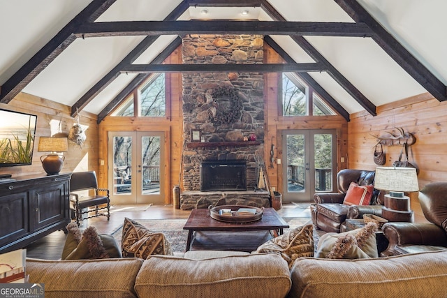 living room with a stone fireplace, high vaulted ceiling, wooden walls, and french doors