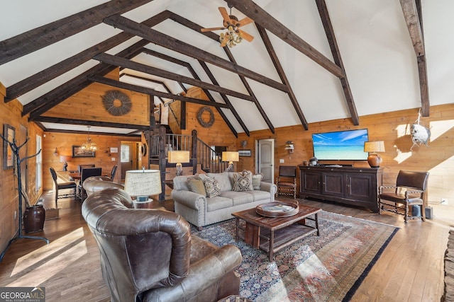 living room with hardwood / wood-style floors, beam ceiling, high vaulted ceiling, ceiling fan with notable chandelier, and wood walls