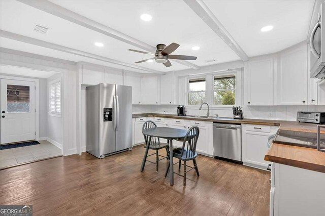 kitchen with appliances with stainless steel finishes, butcher block countertops, sink, white cabinets, and beam ceiling