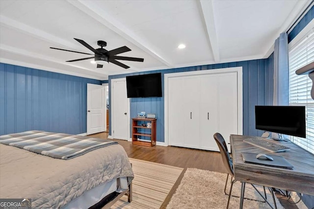 bedroom featuring dark hardwood / wood-style flooring, ceiling fan, multiple closets, and beamed ceiling