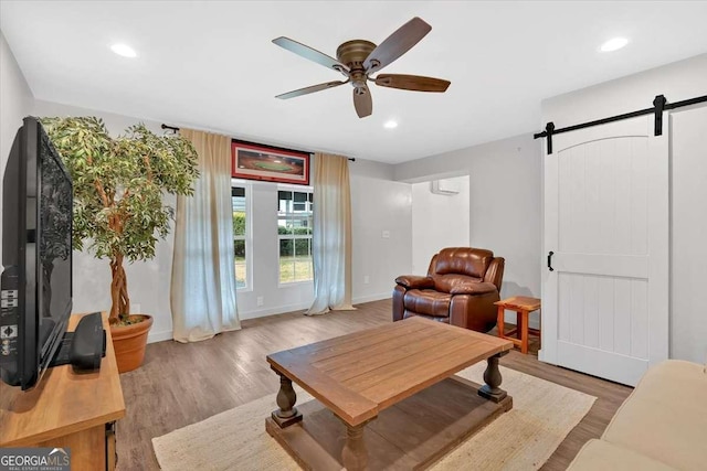 living room with ceiling fan, a barn door, and light hardwood / wood-style flooring