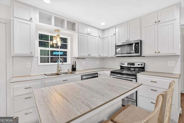 kitchen with appliances with stainless steel finishes, white cabinetry, sink, a kitchen breakfast bar, and hanging light fixtures